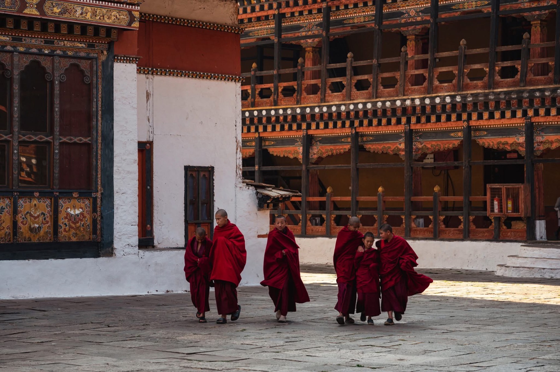 Young monks in crimson robes crossing a sunlit dzong courtyard in Bhutan