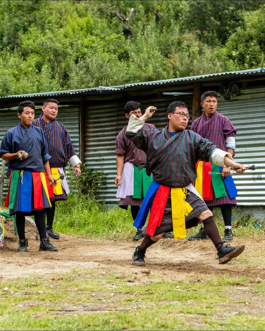 Bhutanese archers in traditional gho competing on a village archery ground